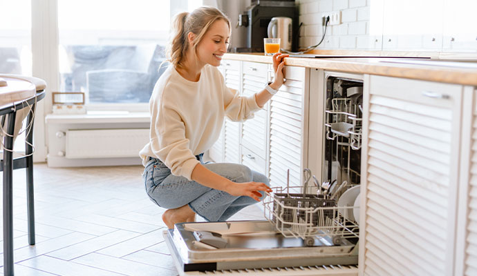 A woman checking the silverware rack of an open dishwasher
