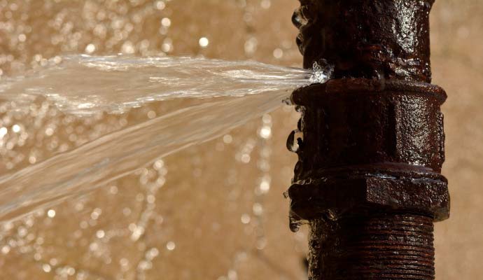 Water spraying from a burst and rusty metal pipe