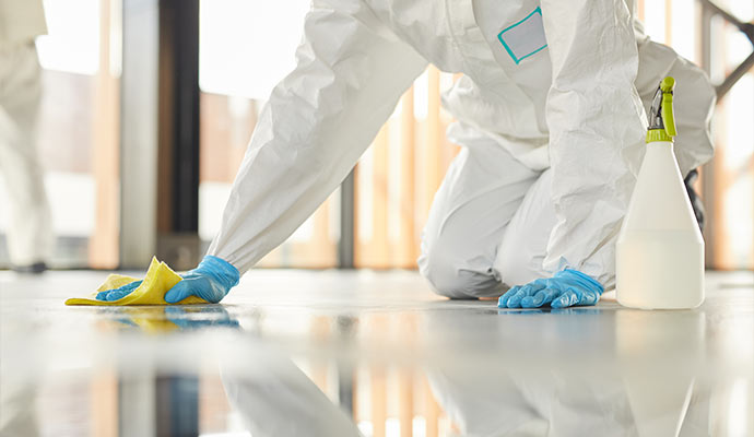 Cleaning specialist in a protective suit and blue gloves wiping a reflective floor with a yellow cloth