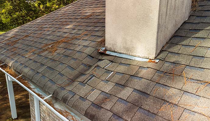 Water damaged and lifting asphalt roof shingles near a stucco chimney