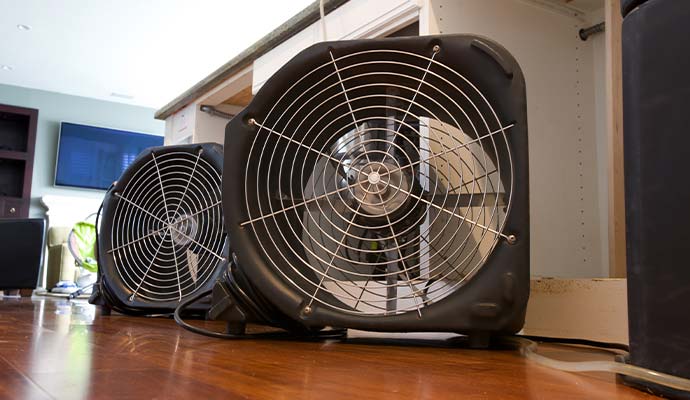 Industrial air movers drying water damage on wooden floor