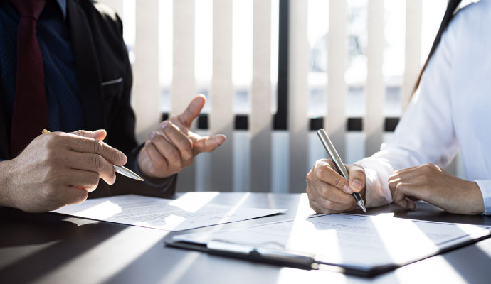 Two professionals in business attire reviewing and signing insurance claim paperwork on a desk