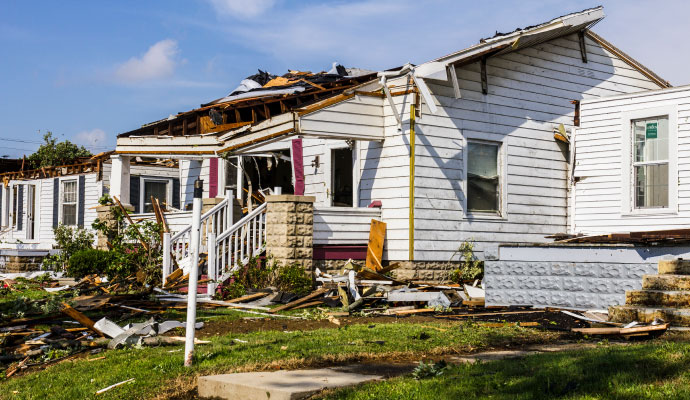 A white residential house with extensive structural damage to the roof and porch following a severe storm