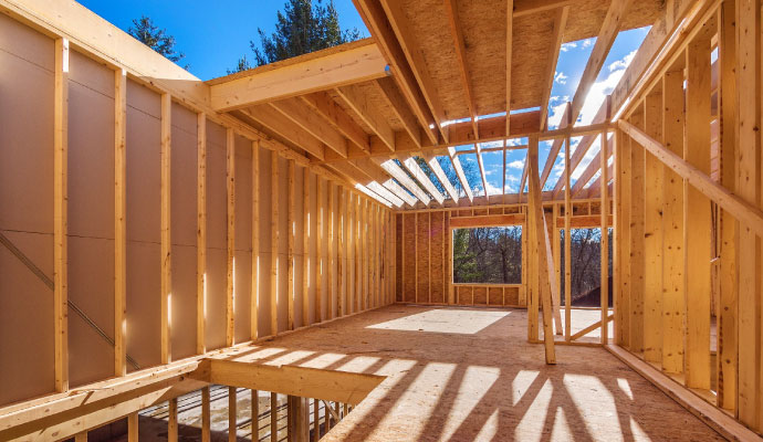 Interior view of a house under reconstruction showing new wooden wall studs and floor joists under a clear blue sky