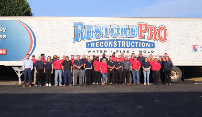 A large group of professional technicians and staff from Restore Pro Reconstruction posing in front of a company trailer