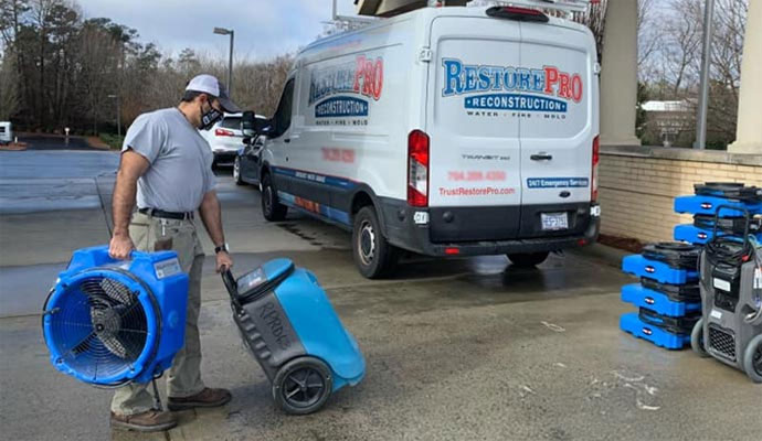 Restore Pro Reconstruction technician unloading air movers and dehumidifiers from a service van at a job site