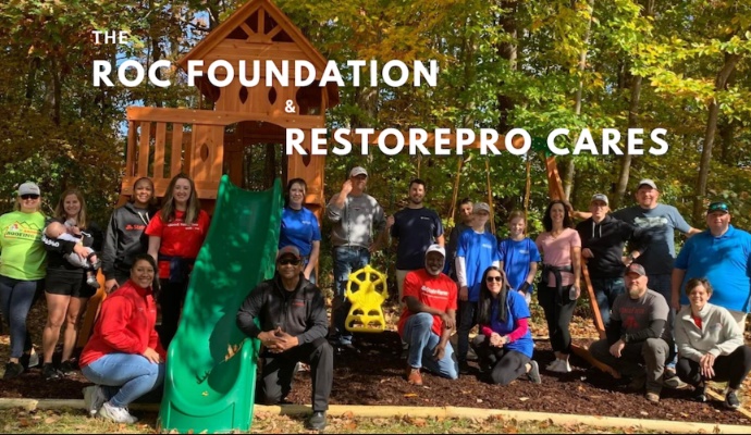 A large group of volunteers from The Roc Foundation and RestorePro Cares posing for a photo in front of a new children's playset