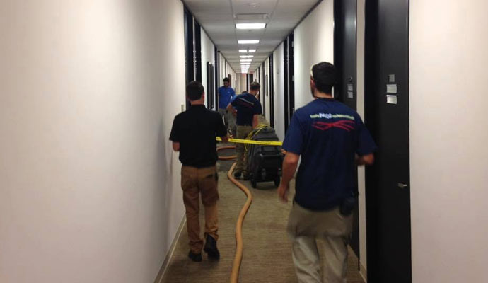 Restoration crew extracting water in hallway