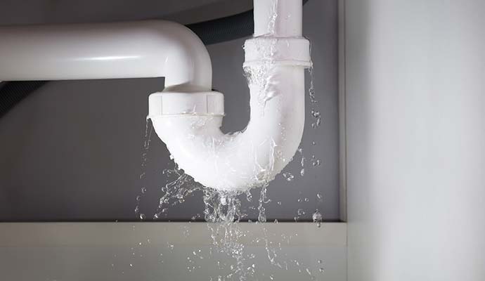 Water dripping from a leaky white plastic P-trap pipe under sink